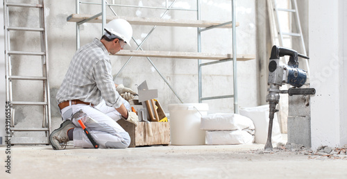 Foto man construction worker work with tool box wear gloves, hard hat and protection glasses at interior building site with scaffolding