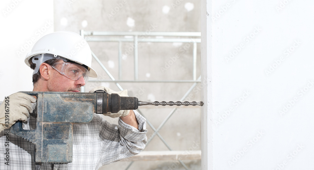 man using an electric pneumatic drill making a hole in wall, professional construction worker with safety hard hat,, gloves and protective glasses. inside construction site
