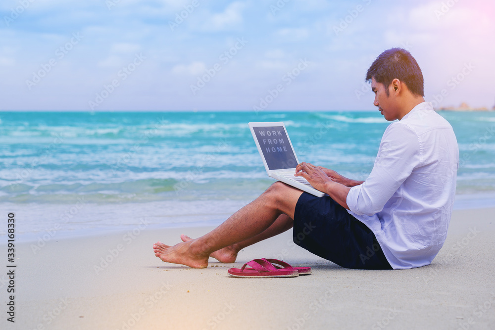 Happiness Handsome man with a shirt working with laptop sitting on the beach beside the sea. Working from home concept