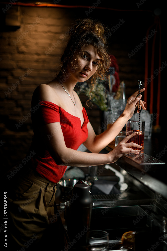 Fototapeta premium Beautiful young woman at bar mixed cocktail by long bar spoon.