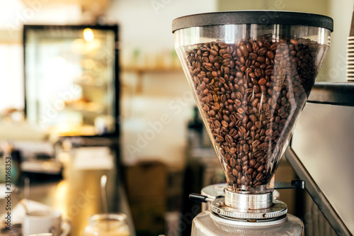 Coffee beans in a big glass grinder machine holder with blurred background of a cafe. © Natalie