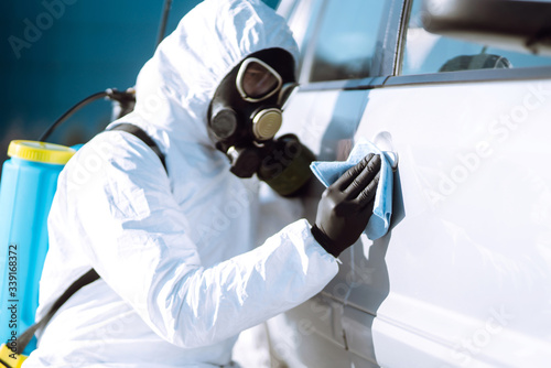Hand of Man in protective suit washing and disinfection handles of a car, to preventing the spread of the epidemic of coronavirus, pandemic in quarantine city. 