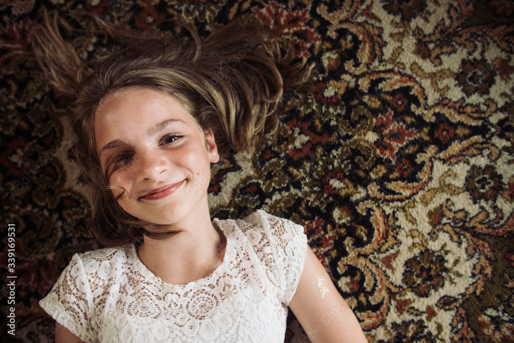 Smiling girl laying on the floor on a Persian carpet in a white dress. Smiling girl laying on the floor on a Persian carpet in a white dress.