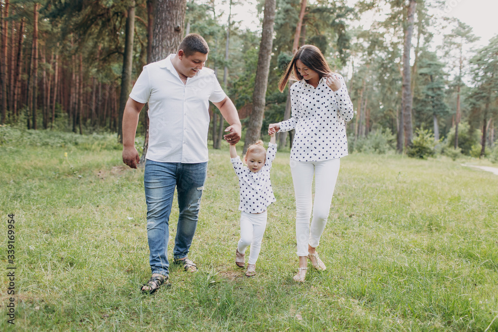 View on toddler. Mother, father hold hands daughter walk in the forest. Young family spending time together on vacation, outdoors. The concept of family summer holiday. selective focus View on toddler. Mother, father hold hands daughter walk in the forest. Young family spending time together on vacation, outdoors. The concept of family summer holiday. selective focus