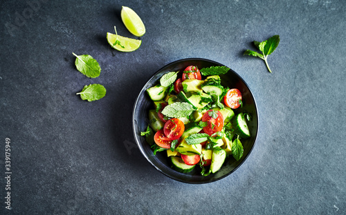 Avocado, tomato and cucumber salad with fresh herbs on dark stone background. Healthy summertime salad. Copy space