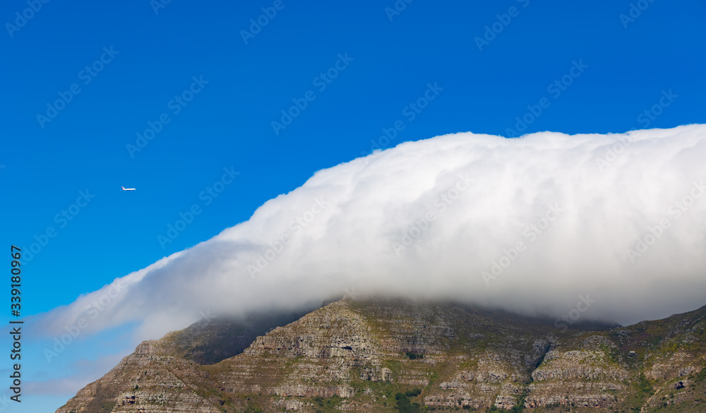 Fototapeta premium Devils Peak on Table Mountain on a cloudy day with a Airplane flying by