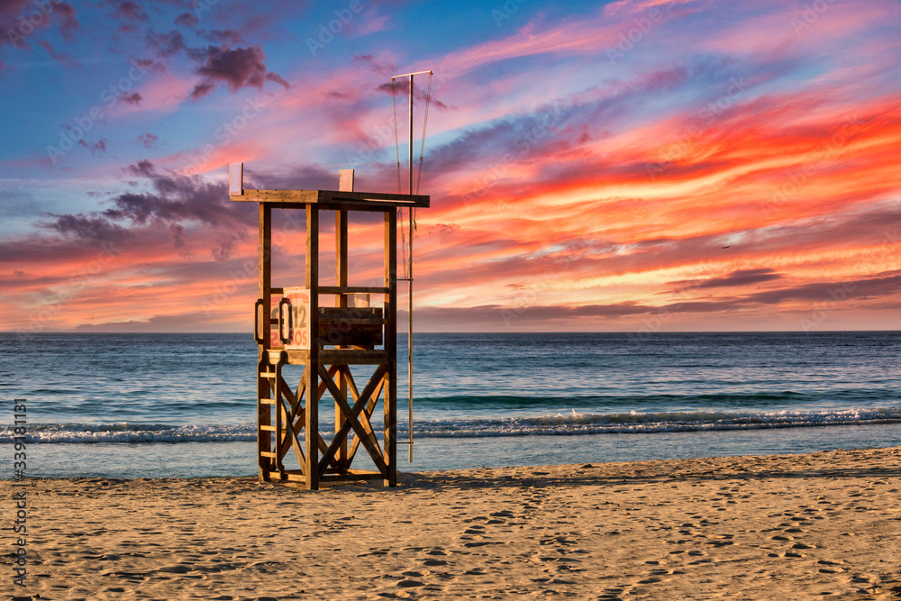 A lifeguard tower stands on the beach on the Mediterranean island of Mallorca with a beautiful colourful sunset
