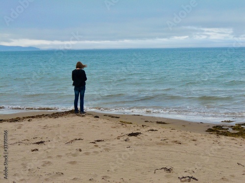 A young woman stands on the edge of a choppy sea on a windy day in Ireland
