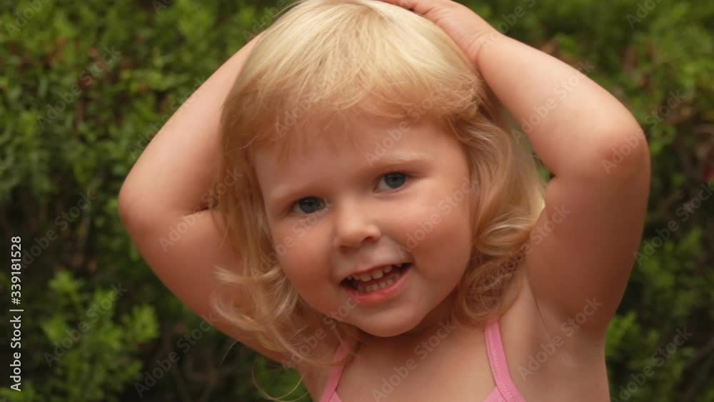 Portrait of a beautiful little blond girl smiling and embracing her head with her hands in sunny park outdoors Portrait of a beautiful little blond girl smiling and embracing her head with her hands in sunny park outdoors