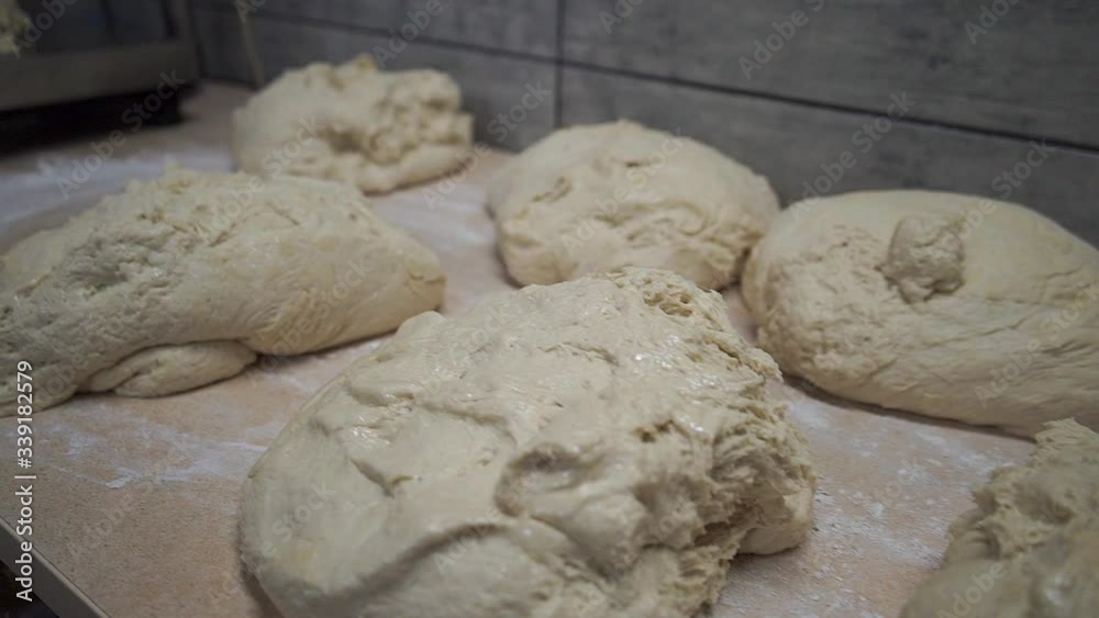 Closeup of kneading dough on kitchen table, side view. Mature woman put sticky dough in flour on table and start kneading it. Closeup of kneading dough on kitchen table, side view. Mature woman put sticky dough in flour on table and start kneading it.