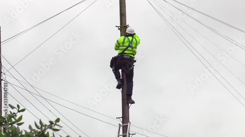 An unidentifiable telephone engineer wearing a safety helmet and high visibility jacket, loosening safety ropes and carefully climbing down a telegraph pole, with cables in all directions. photo