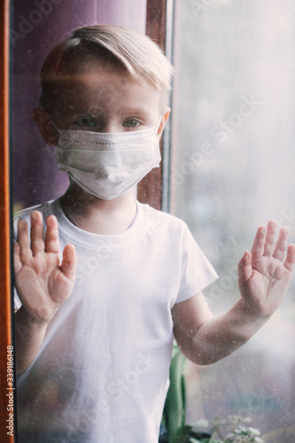 Stay at home quarantine coronavirus pandemic prevention. Sad child both in protective medical masks near windows and looks out window. View from street. Prevention epidemic. Coronavirus concept