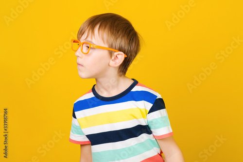 Curious boy looking aside and listens somethink. Smart boy in glasses over yellow background. photo