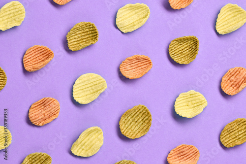 Potato chips colorful pattern on purple background. Vegan spinach, tomato, carrot snack chip. Crisps potato chips wallpaper, top view. Creative concept, fashionable trendy flat lay