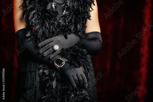 Beautiful woman standing in old historical 20th century in flapper dress with fringe, feathers boa on red background. Details of Gatsby costume, treasure jewelry.