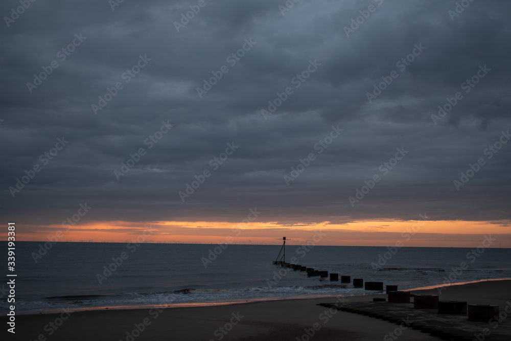 sunrise at the coast in mablethorpe uk. moody skies and blue sea