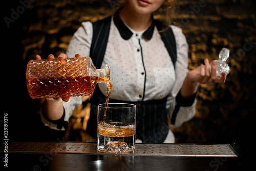 Photo Close-up barman lady carefully pours alcoholic drink from bottle into glass