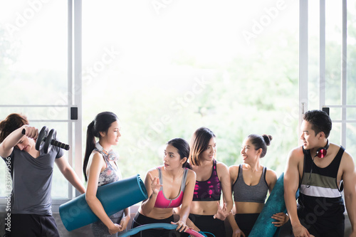 A group of healthy men and women are having fun chatting, wearing exercise clothes and headphones and carrying exercise equipment in the morning exercise room.