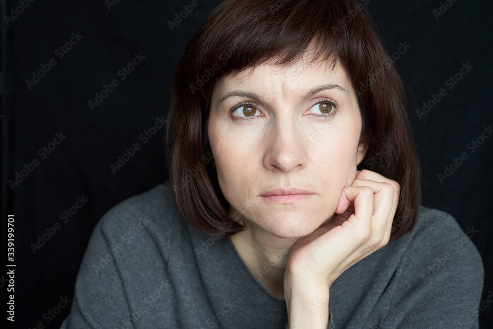 Mature, middle-aged woman looks anxiously ahead, chin propped on hand. Close-up portrait. Mature, middle-aged woman looks anxiously ahead, chin propped on hand. Close-up portrait.
