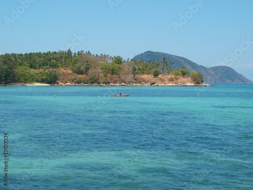 Beautiful transparent azure water. Tropical island, coast, boat in the distance. Panoramic sea landscape on a sunny sultry day. Hills on the horizon, sandy shore, stones dark silhouettes on the depth