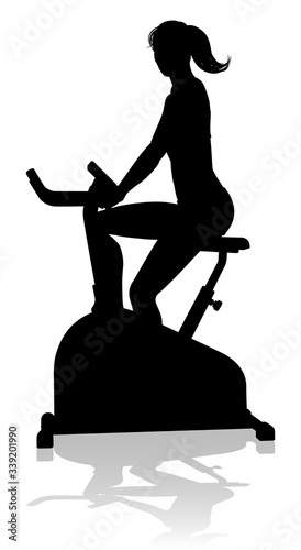 A woman in silhouette using a stationary exercise spin bike piece of gym equipment fitness machine