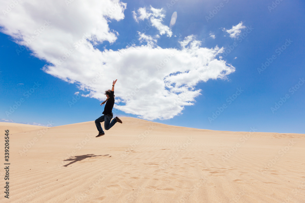 Unrecognizable man jumping on the top of a desert dune. New experiences traveling around the world. Man enjoying freedom. Travel and holidays concept. Maspalomas natural landscape in Canary Island. Unrecognizable man jumping on the top of a desert dune. New experiences traveling around the world. Man enjoying freedom. Travel and holidays concept. Maspalomas natural landscape in Canary Island.