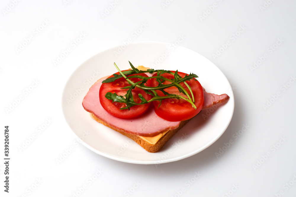 Sandwich of balyk, cheese, bread, tomatoes and arugula on a white plate on a plate