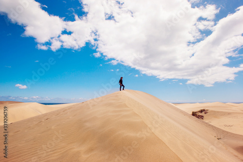 Panoramic landscape with man on the top of a desert dune. New experiences traveling around the world. Man enjoying freedom. Travel and holidays concept. Maspalomas natural landscape in Canary Island.