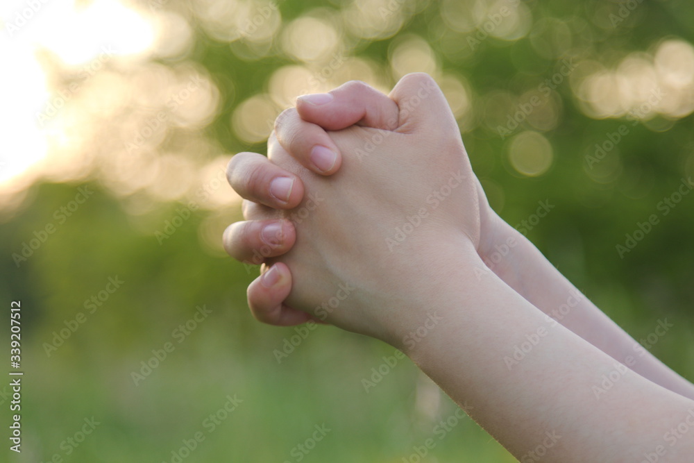 Closeup of woman's hands praying outdoors with green nature background Closeup of woman's hands praying outdoors with green nature background