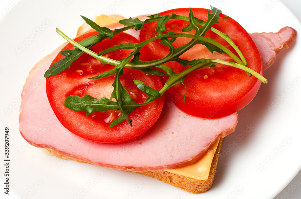 Sandwich of balyk, cheese, bread, tomatoes and arugula on a white plate on a plate flat lay