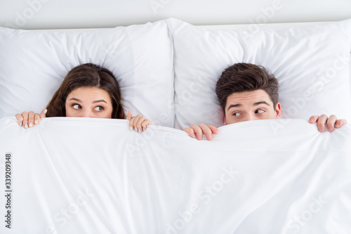 High angle above view photo of pretty lady husband guy couple lying sheets bed covering blanket faces morning romantic playful look eyes honeymoon wear pajama room indoors