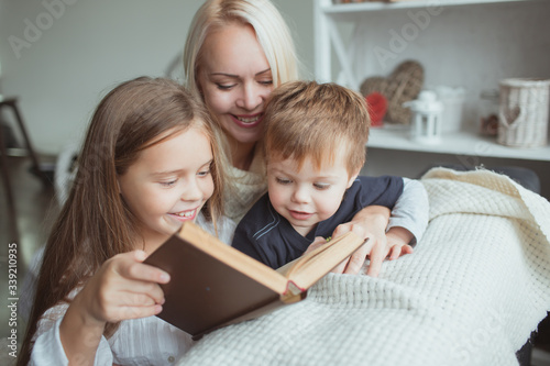 Mom and daughter and son read a book at home.