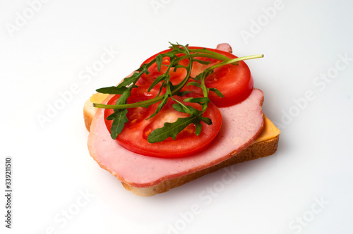 A sandwich of balyk, cheese, bread, tomatoes and arugula on a white plate view from the side and from the top