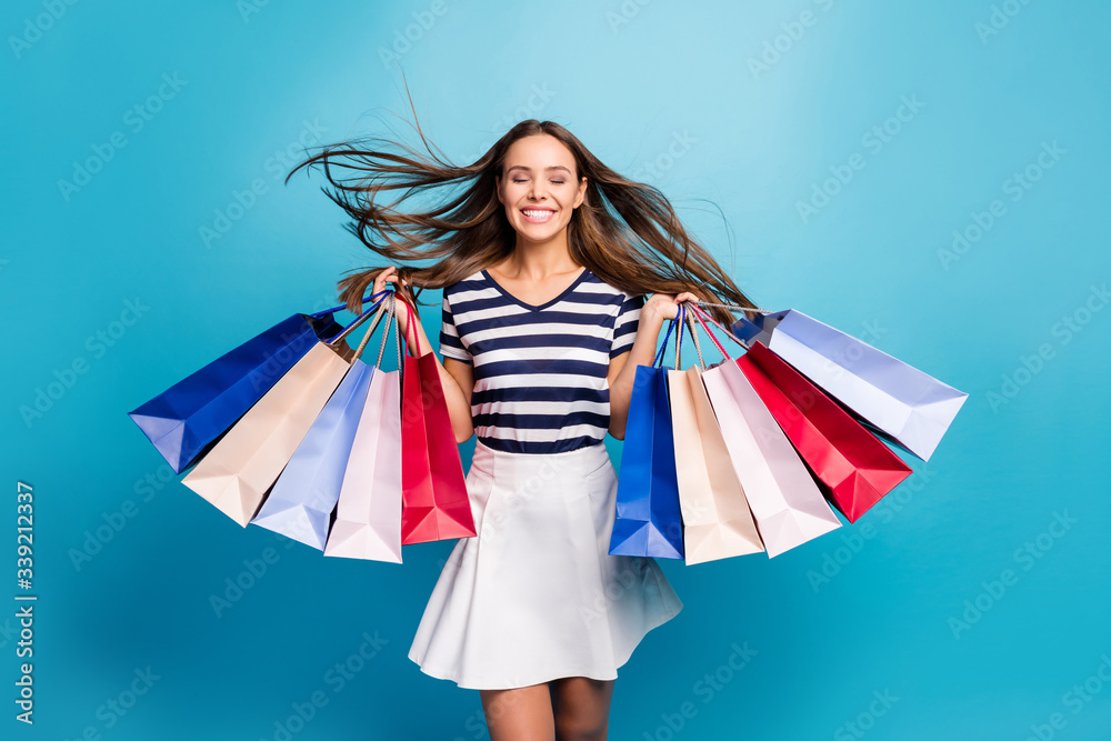 Photo of charming lady traveler walk enjoy shopping center carry many packs hairstyle flight eyes closed satisfied shopper wear white striped t-shirt skirt isolated blue background