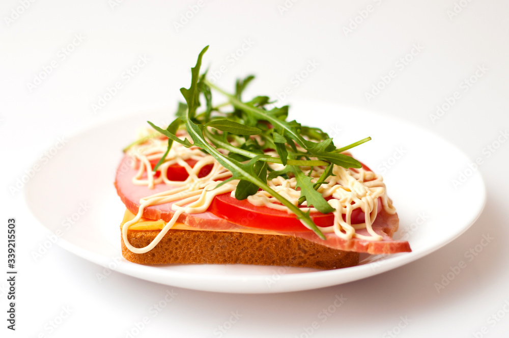 Sandwich of bread for toast, sturgeon, tomatoes, arugula, cheese and mayonnaise on a white background in a plate