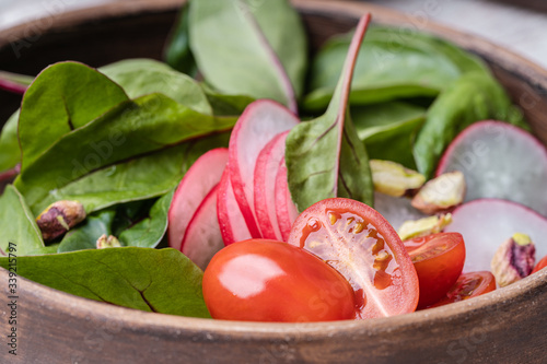 Fresh salad bowl with green chard leaves, sliced radish, cherry tomatoes and pistachios
