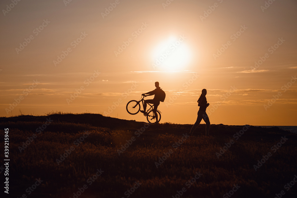 silhouette of men on a bicycle and a woman running towards him against a sunset