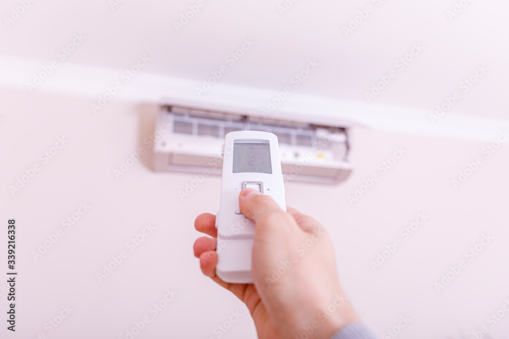 Close-up Of Young man hand operating air conditioner with remote control. Hand with remote control directed on the conditioner. Close-up Of Young man hand operating air conditioner with remote control. Hand with remote control directed on the conditioner.