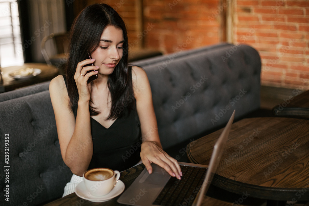 Business woman working on a laptop, using phone and drinking coffee in a cafe. Business woman working on a laptop, using phone and drinking coffee in a cafe.