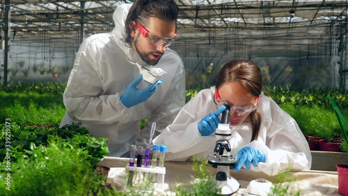 Two biologists are holding a research with a microscope