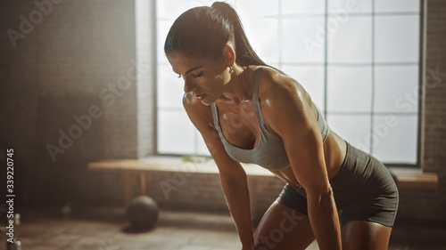 Portrait of a Beautiful Strong Fit Brunette Wiping Sweat from Her Face in a Loft Industrial Gym with Motivational Posters. She's Catching Her Breath after Intense Fitness Training Workout. Warm Light.
