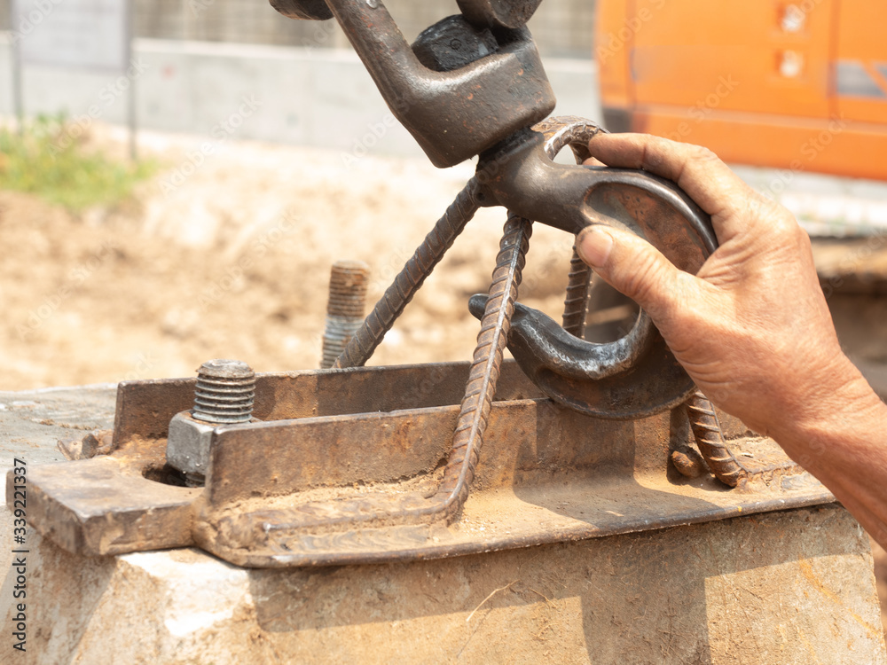 The right hand of the worker is holding the hook to fasten on the bracket for lifting the material to move with the crane. The right hand of the worker is holding the hook to fasten on the bracket for lifting the material to move with the crane.