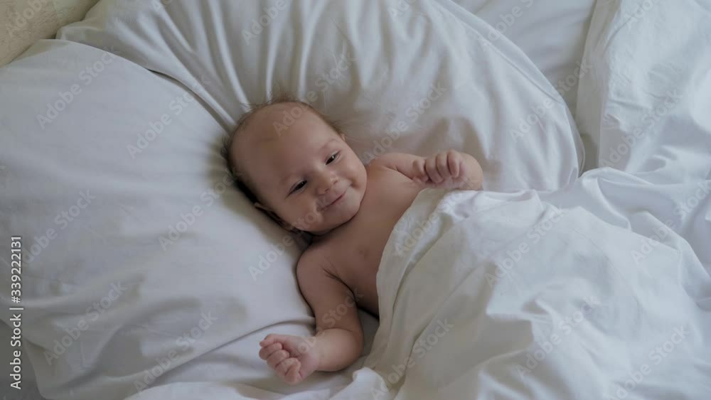 Portrait Of Funny Little Baby Lying In Bed On Pillow Under Blanket And Smiling Portrait Of Funny Little Baby Lying In Bed On Pillow Under Blanket And Smiling