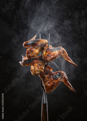 barbecue chicken wings fried on a barbecue mounted on a meat fork