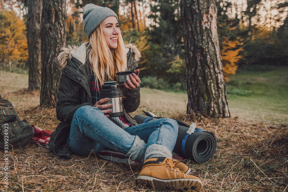 Hiking and travel along in the forest. Concept of trekking, adventure and seasonal vacation. Young woman with thermos sitting in woods. Hiking and travel along in the forest. Concept of trekking, adventure and seasonal vacation. Young woman with thermos sitting in woods.
