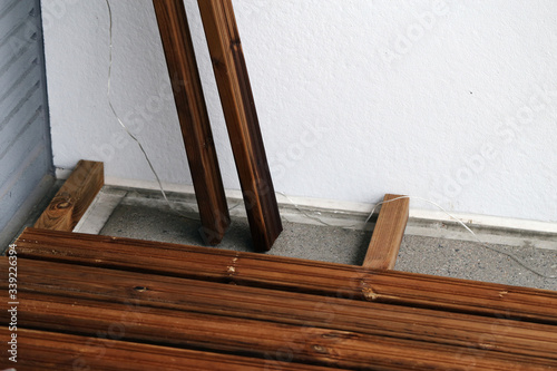 DIY building a porch / balcony floor with brown wooden planks in Espoo, Finland, spring, 2020. In this photo you can see the floor in progress and cement under it. Closeup color photo.