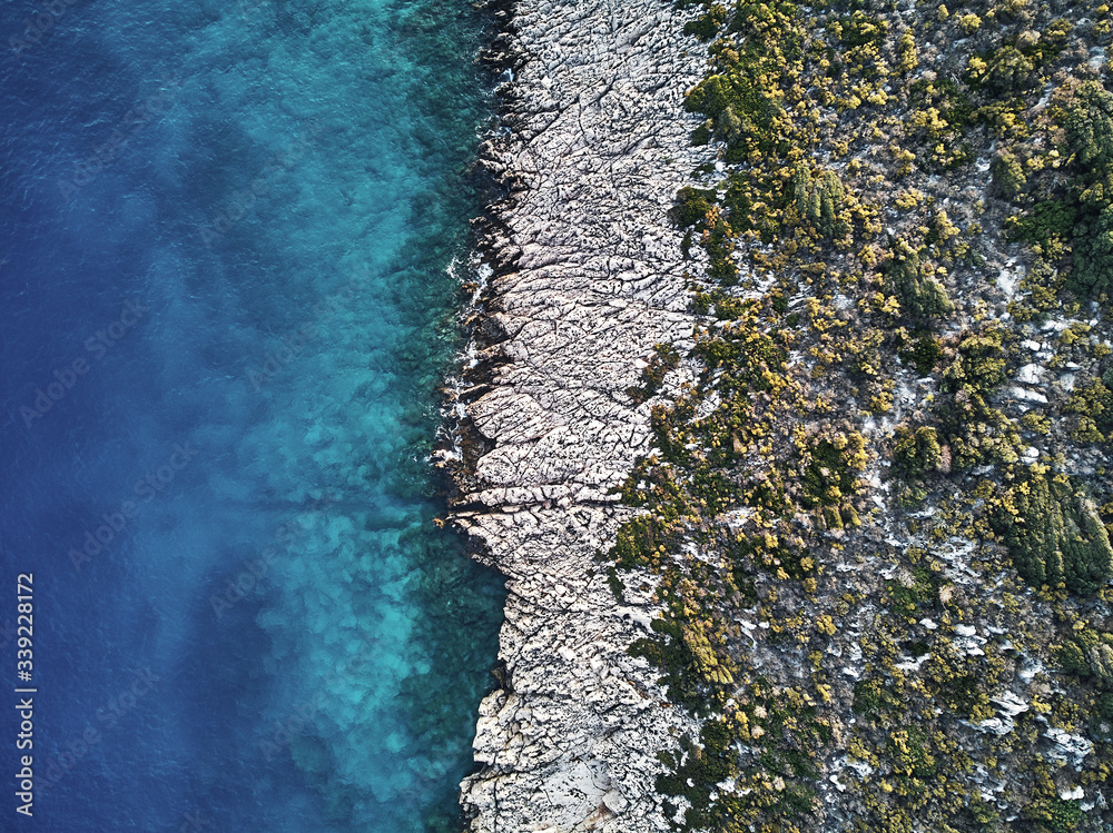 top drone view of a stony coast clashing into the blue ocean sea. Structure and Pattern in artistic way of the sharp rocks in the water. Aerial top shot on warm summer waves. top drone view of a stony coast clashing into the blue ocean sea. Structure and Pattern in artistic way of the sharp rocks in the water. Aerial top shot on warm summer waves.