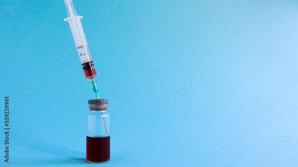 Coronavirus flu and pandemic vaccines, syringe and vial with red liquid on a blue background. medical concept, subcutaneous injection, treatment of the disease. Copy space for text or logo Coronavirus flu and pandemic vaccines, syringe and vial with red liquid on a blue background. medical concept, subcutaneous injection, treatment of the disease. Copy space for text or logo