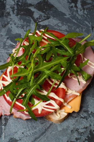 Appetizing sandwich with ham or balyk, arugula, cheese, tomatoes and mayonnaise on a gray background top view flat lay