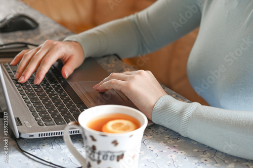 woman's hands on a computer keyboard next to tea with a lemon theme of remote work in a pandemic